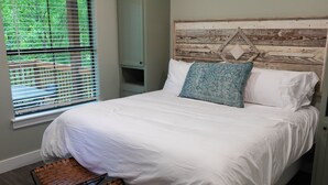 A neatly made bed with white linens, a patterned pillow, and a rustic headboard. - Cozy, Spacious, and Right on the Banks of Rocky Creek, Two Creeks Crossing Resort (Livingston)