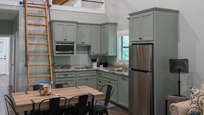 A compact kitchen with a built-in microwave, stainless steel refrigerator, and a dining area with a wooden table and chairs. - Cozy, Spacious, and Right on the Banks of Rocky Creek, Two Creeks Crossing Resort (Livingston)