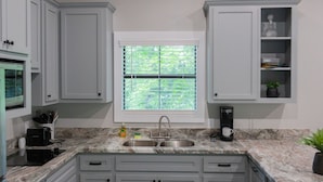 A kitchen with white cabinets, a sink, a window with blinds, a coffee maker, and a microwave. - A Cozy Getaway Right on the Water, Two Creeks Crossing Resort (Livingston)