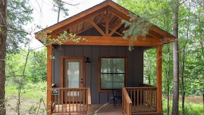 A wooden cabin with a porch, a door, and a window. - A Cozy Getaway Right on the Water, Two Creeks Crossing Resort (Livingston)