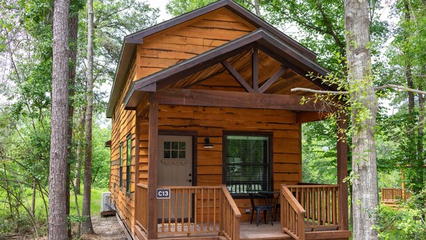 A wooden cabin with a porch, a door, and a window. - Cozy, Spacious, and Right on the Banks of Rocky Creek, Two Creeks Crossing Resort (Livingston)