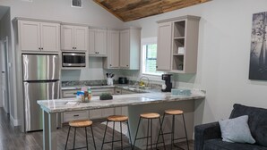 Una cocina moderna con armarios blancos, electrodomésticos de acero inoxidable, encimera de mármol y taburetes de bar.