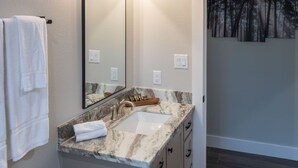 Un baño con lavamanos de mármol, un espejo grande y un cuadro de un bosque en la pared.
