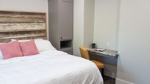 Un dormitorio con cama, cabecera de madera, escritorio con silla y un mueble pequeño.