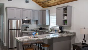Una cocina moderna con gabinetes grises, electrodomésticos de acero inoxidable, encimera de mármol y una zona con taburetes de bar.