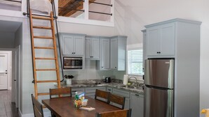 Une cuisine avec des meubles de couleur bleu clair, un réfrigérateur en acier inoxydable, une table à manger en bois avec des chaises, et une échelle en bois.