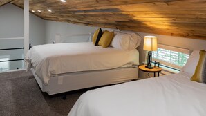 Une chambre avec deux lits, un plafond en bois, une petite table avec une lampe et une fenêtre avec des stores.
