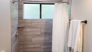 Une douche avec une porte en verre, une fenêtre au-dessus et un porte-serviettes avec des serviettes.