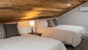 Une chambre avec deux lits, une table de chevet avec une lampe, un plafond en bois et un appareil de climatisation.