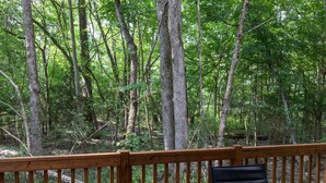 Une terrasse en bois avec deux chaises noires donnant sur une zone boisée.