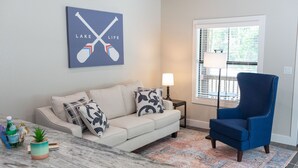 Un salon avec un canapé, un fauteuil bleu, une table basse, une lampe et un tableau accroché au mur.