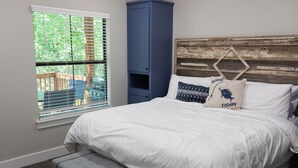 Une chambre à coucher avec un lit, un banc, une fenêtre avec des stores et une armoire bleue.