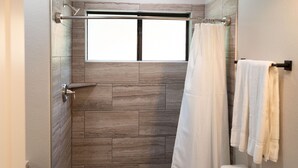 Une douche avec fenêtre, des toilettes et un porte-serviettes.