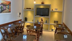 Un comedor con mesas y sillas de madera, un televisor de pantalla plana y objetos decorativos en estanterías.