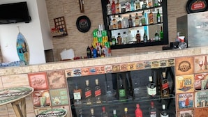 Una zona de bar con diversas botellas de licor, un televisor montado en la pared y una mesa de madera con un posavasos de Heineken.