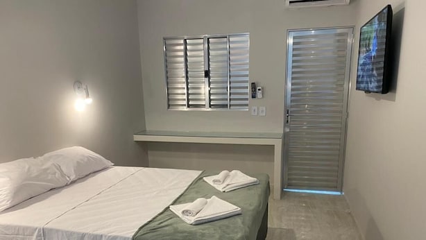 Un dormitorio con dos camas, una ventana con persianas, una puerta con manija y un televisor montado en la pared.