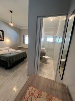 Quarto de hotel moderno com cama, mesa de cabeceira e vista para o banheiro.