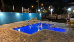 Piscina con baldosas de piedra y un elemento acuático azul, rodeada por un muro azul e iluminación exterior.