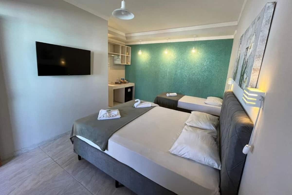 Habitación de hotel con una cama grande, un televisor de pantalla plana en la pared y una pequeña kitchenette, además de una pared verde decorativa.