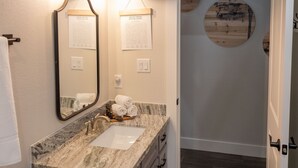 Un baño con un lavamanos de mármol, un espejo, dos juegos de palabras enmarcados en la pared y un detalle circular de madera en la pared.
