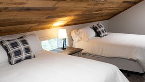 Un dormitorio con dos camas, techo de madera y una mesita de noche con lámpara.