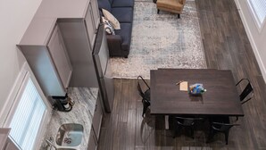 Una cocina moderna con armarios grises, una mesa de comedor de madera oscura con cuatro sillas, un sofá gris y un sillón color beige.