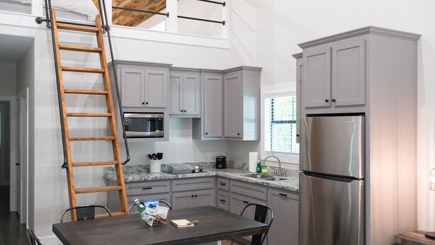 Una cocina moderna con armarios grises, un refrigerador de acero inoxidable, un microondas y un comedor con mesa y sillas.