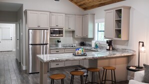 Een moderne keuken met witte kastjes, roestvrijstalen apparatuur, een marmeren aanrecht en houten krukken.