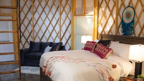 A bedroom with a wooden lattice wall, a bed with multiple pillows and a white comforter, a wooden nightstand with a lamp, and a small plant. - Close to nature, but with all the modern amenities, Two Creeks Crossing Resort (Livingston)