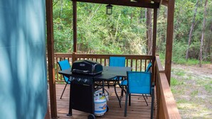 A covered outdoor deck with a grill, chairs, and a propane tank. - Close to nature, but with all the modern amenities, Two Creeks Crossing Resort (Livingston)