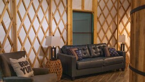 A cozy living room with a dark leather sofa, a wooden lattice wall, a woven side table, and a patterned rug. - Close to nature, but with all the modern amenities, Two Creeks Crossing Resort (Livingston)