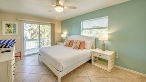 A bedroom with a bed, nightstands, a ceiling fan, a window with blinds, and a view of the outdoors. - 110 Bahia #3 Pet Friendly Canal Unit with Pool (Fort Myers Beach)