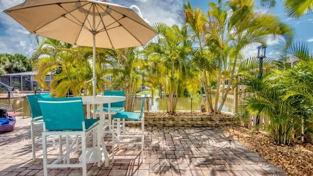 Un patio con una mesa, sillas, un paraguas grande y una piscina.