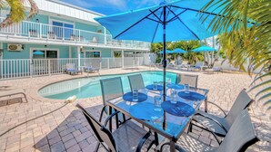 A poolside area with a table and chairs, a pool, and a building with balconies. - 110 Bahia #3 Pet Friendly Canal Unit with Pool (Fort Myers Beach)