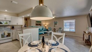 Cocina moderna con armarios blancos, comedor con una mesa dispuesta para cuatro personas y una lámpara colgante grande.