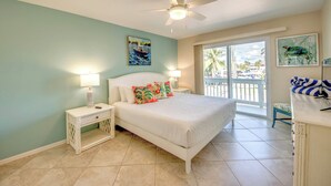 A bedroom with a bed, two bedside lamps, a ceiling fan, and a view of the outside.