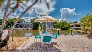 A patio with a table and chairs, a covered seating area, a body of water, and palm trees.