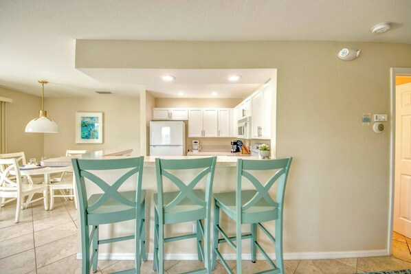 A modern kitchen with white cabinets, a refrigerator, and a coffee maker. There is a dining area with a table and chairs.