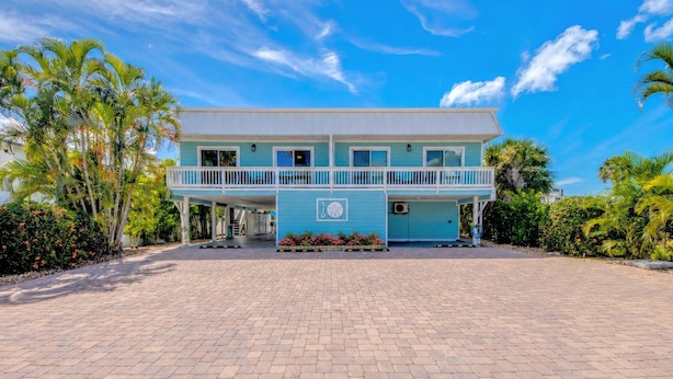 Un bâtiment à deux étages doté d’un balcon, d’une allée pavée et d’un aménagement paysager de style tropical.