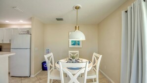 Une cuisine compacte avec un coin repas, comprenant un réfrigérateur blanc, une table avec des chaises et un luminaire suspendu.