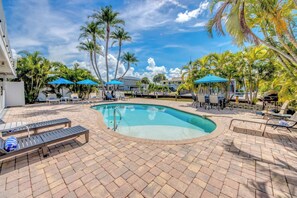 A swimming pool with lounge chairs and umbrellas, surrounded by palm trees and a clear sky.
