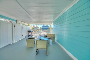 A covered patio area with wicker furniture and a table, white doors, and a view of buildings in the background.