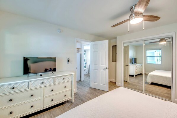 A bedroom with a television, a dresser, a ceiling fan, and a mirror.
