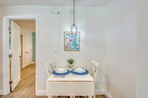 Un área de comedor con una mesa blanca para dos personas, una lámpara colgante y una obra de arte colorida en la pared.
