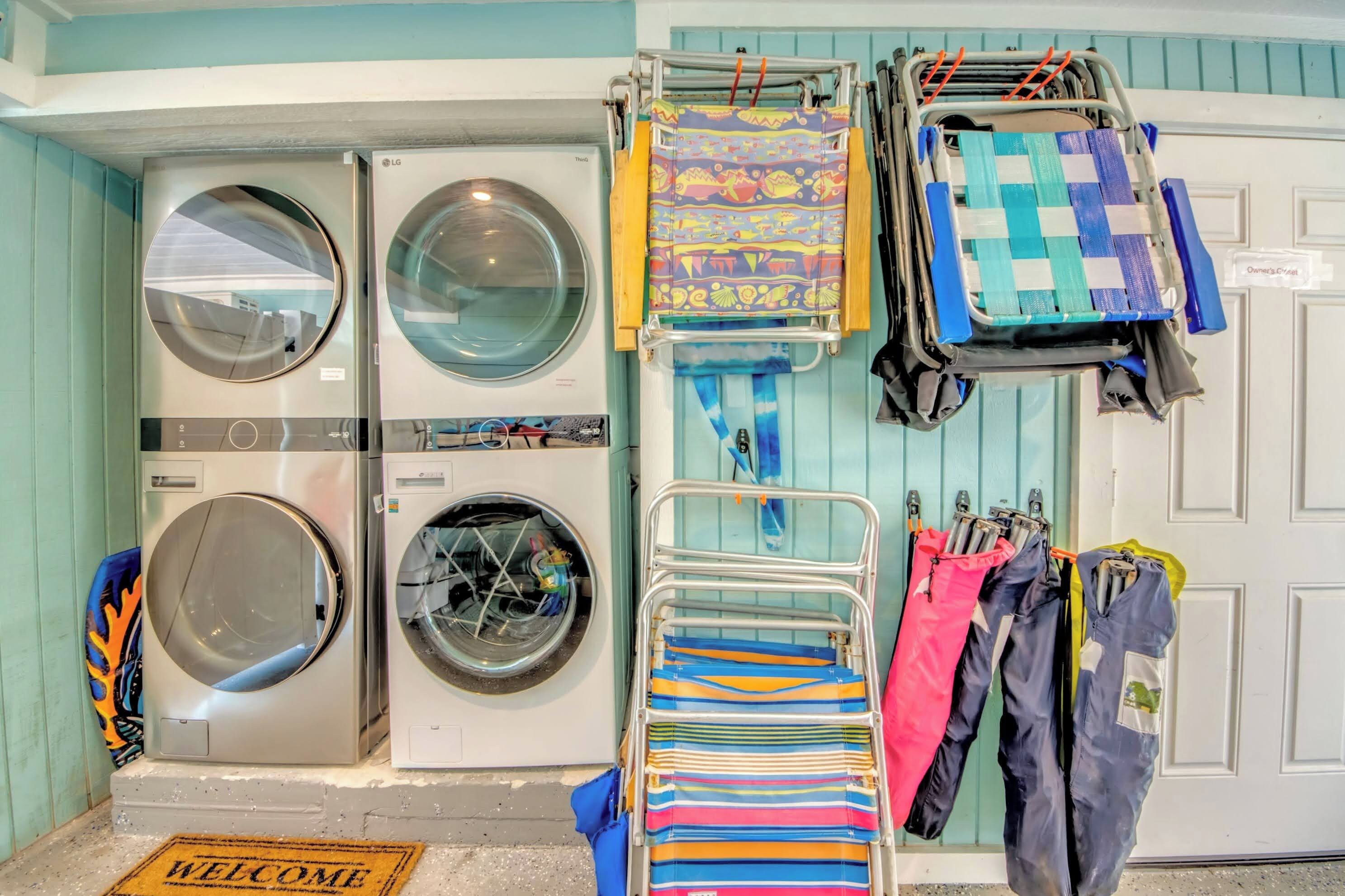 Un área de lavandería con dos lavadoras, un tendedero con ropa de colores y una puerta con felpudo que dice 'Welcome'.