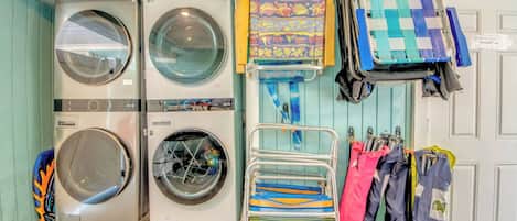 A laundry area with two washing machines, a drying rack with colorful clothes, and a door with a 'Welcome' mat.