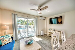 A hotel room with a balcony, a ceiling fan, a flat-screen TV, a desk with a chair, and a bed with a blue cover.