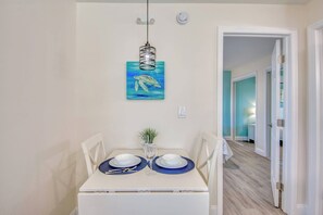 A dining area with a table set for two, a hanging light fixture, and a painting of a sea turtle on the wall.