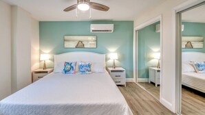 Une chambre à coucher comprenant un lit, deux tables de chevet avec des lampes, un ventilateur de plafond, un appareil de climatisation et un grand miroir.