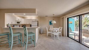 A modern kitchen with white cabinets, a dining area with white chairs, and a large sliding glass door leading to an outdoor patio. - 110 Bahia Entire Pet Friendly Canal Home with Pool (Fort Myers Beach)